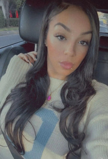 A car selfie showing long dark wavy hair and a cream-colored sweater.