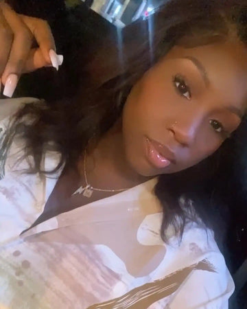 A close-up selfie showing someone wearing a white patterned top and delicate necklace.