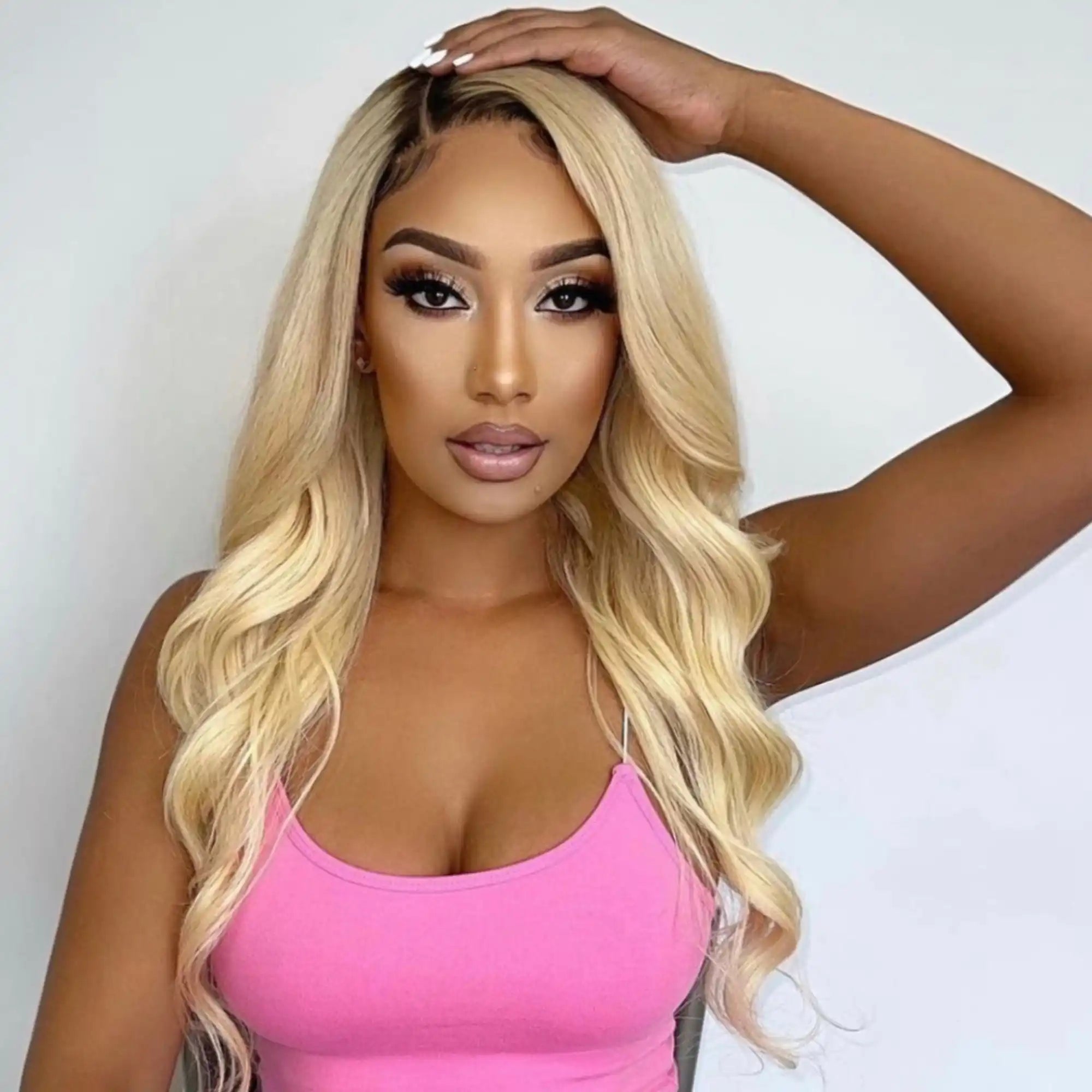 A glamorous portrait featuring long blonde wavy hair, flawless makeup, and a bright pink tank top.