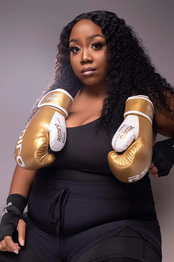 Gold and white boxing gloves worn by someone in a black outfit.