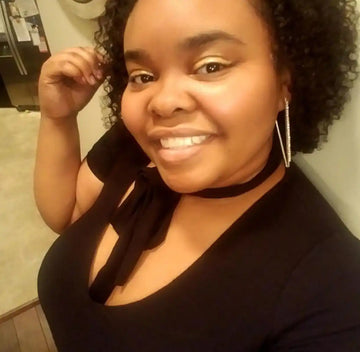 A selfie showing a bright smile, natural curly hair, and dangling silver earrings.